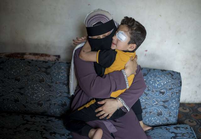 Eine Person in einem Niqab umarmt ein Kind auf einem Sofa in einem Innenraum.